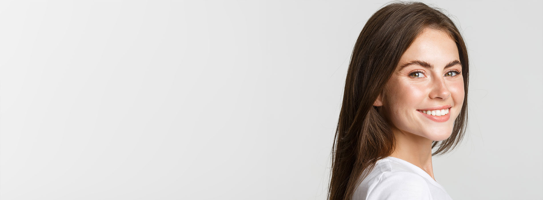 The image is a photograph of a woman with light skin, smiling at the camera. She appears to be in her late twenties or early thirties and has long hair. Her eyes are looking directly at the camera, and she is holding up her index finger near her mouth as if she s making a point or emphasizing something. The background is plain and light-colored, which suggests that this could be a stock photo used for various purposes such as advertising, personal branding, or lifestyle content.